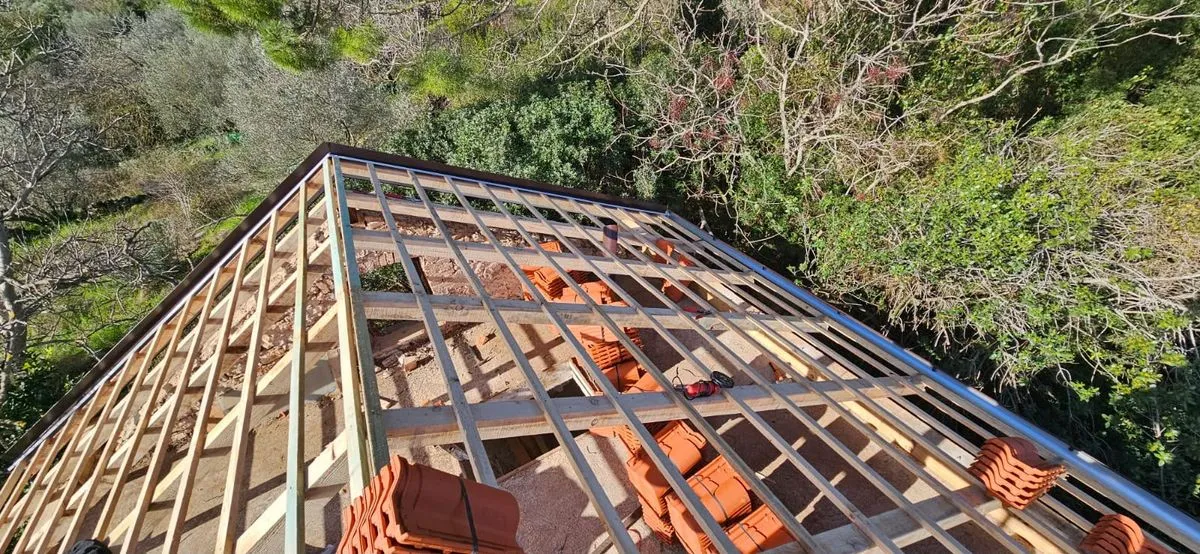 Structură metalică de acoperiș montată peste zidărie, cu pachetele de țiglă ceramică pregătite deasupra