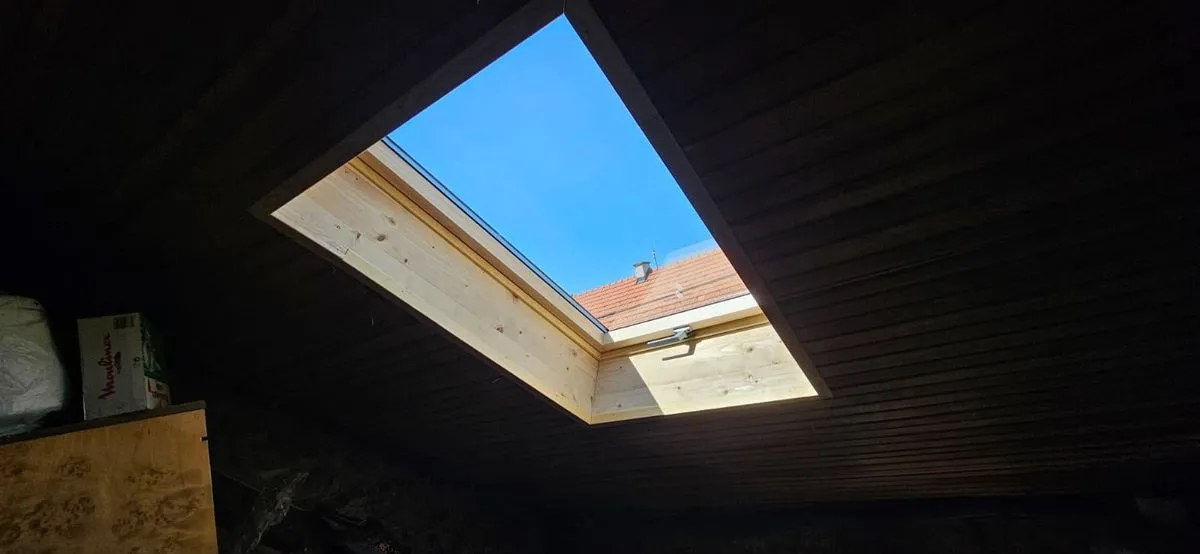 Fereastră de mansardă văzută din interior, cu ancadramentul de lemn finisat